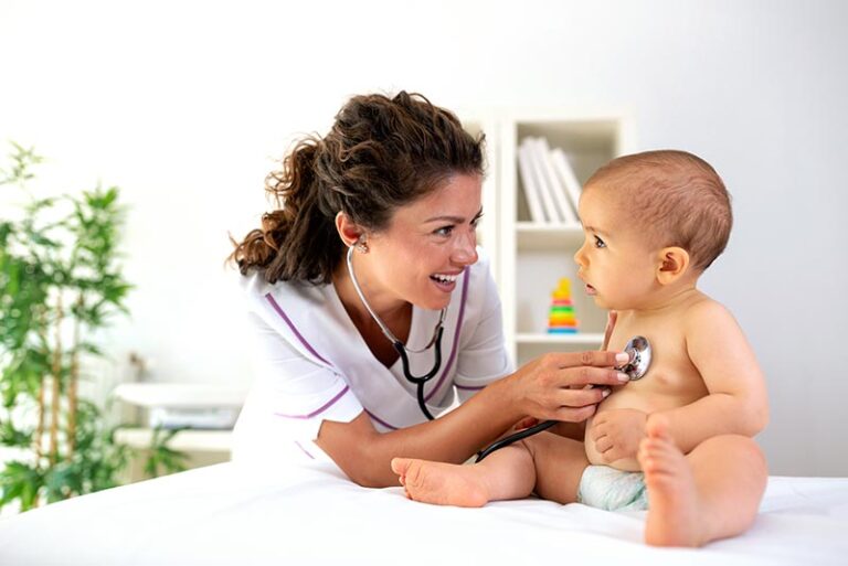 Pediatrician checking the heartbeat of a baby sitting on an examining table.