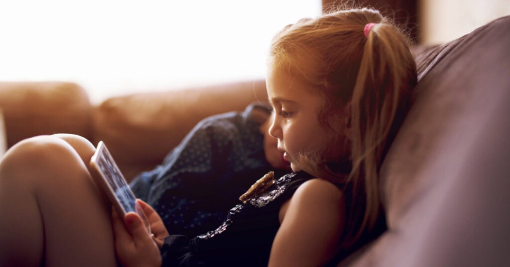 Little girl sitting on couch and using tablet.
