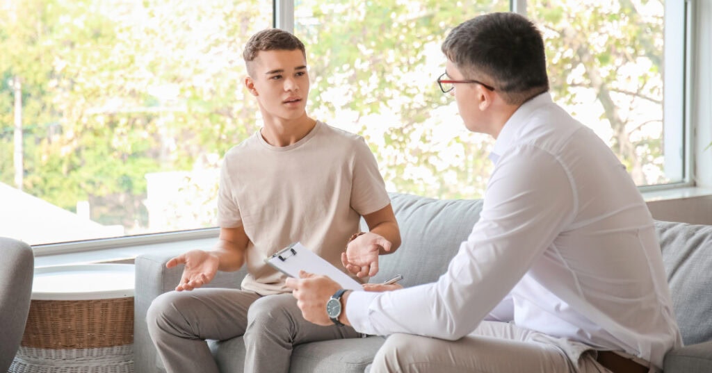 Pediatrician sitting on couch with teenager during appointment.