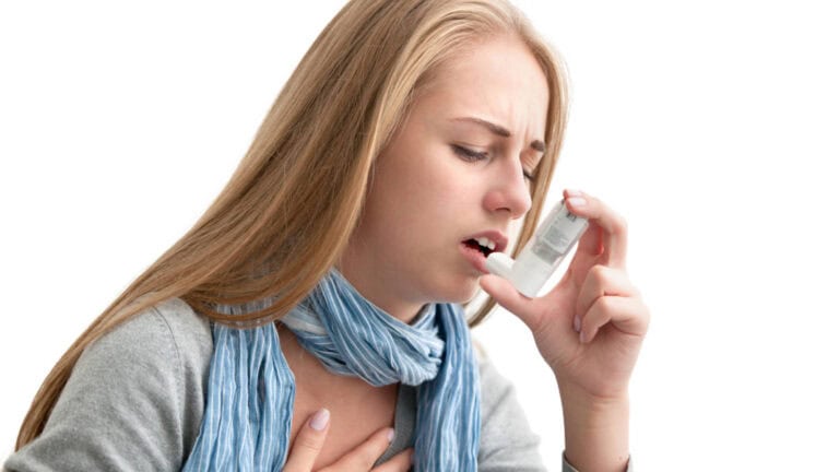 Teen with asthma holding her chest while she uses an inhaler.